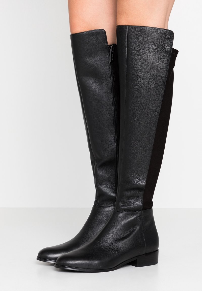 Botas de piel negra hasta la rodilla con un acabado suave y cremallera lateral; presentan paneles de ante para añadir textura y un tacón bajo y cuadrado.