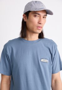 Blå bomull T-skjorte med rund hals og korte ermer, med en liten brodert logo på brystet. Kombineres med stripete caps.
