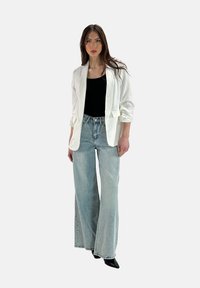 Blazer bianco con maniche rimboccate, abbinato a una canotta nera e jeans a gamba larga azzurri in vita alta. Scarpe nere a punta.