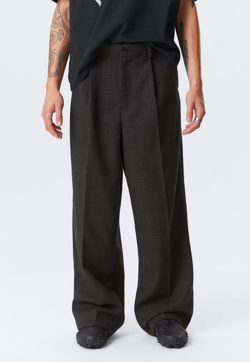 Temno karirane hlače s sproščenim krojem, ki imajo visok pas, eno gumbasto zapiranje in stranske žepe. Tkanina ima teksturiran vzorec.