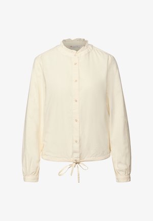 Valkoinen nappikauluspaita, jossa on röyhelökaulus, pitkät hihat ja vyötäröllä sidottava nauha. Valmistettu pehmeästä, kevyestä kankaasta, jolla on sileä rakenne.