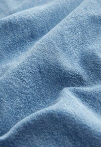 Tissu en denim bleu clair doux avec une texture de sergé visible et des plis doux créant des ombres et de la profondeur.