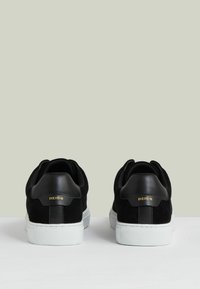 Sneaker in suede nera con dettagli in pelle nera e suola in gomma bianca. Marchio dorato sul tallone. Vista posteriore che mostra un design arrotondato.