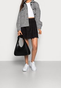 Grijze textuur jas met ronde knopen, witte crop top, zwarte golvende rok, zwarte schoudertas en witte sneakers.