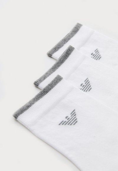 Baldos su baltomis kojinėmis ir pilkais raukiniais, su mažomis pilkomis dryžuotomis logotipomis ant kiekvienos kojinės. Sklandus paviršius ir standartinė kulkšnies ilgis.