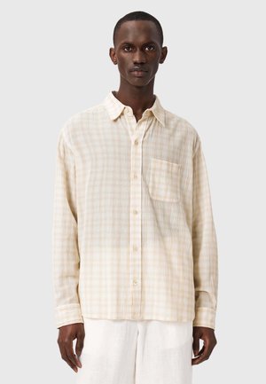 Chemise boutonnée couleur crème à motif à carreaux, avec une poche poitrine, des manches longues et une coupe décontractée, fabriquée à partir d'un tissu léger et texturé.