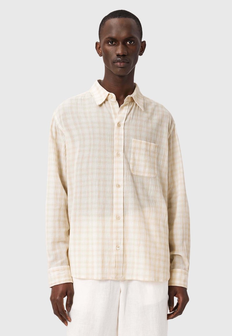 Chemise boutonnée couleur crème à motif à carreaux, avec une poche poitrine, des manches longues et une coupe décontractée, fabriquée à partir d'un tissu léger et texturé.