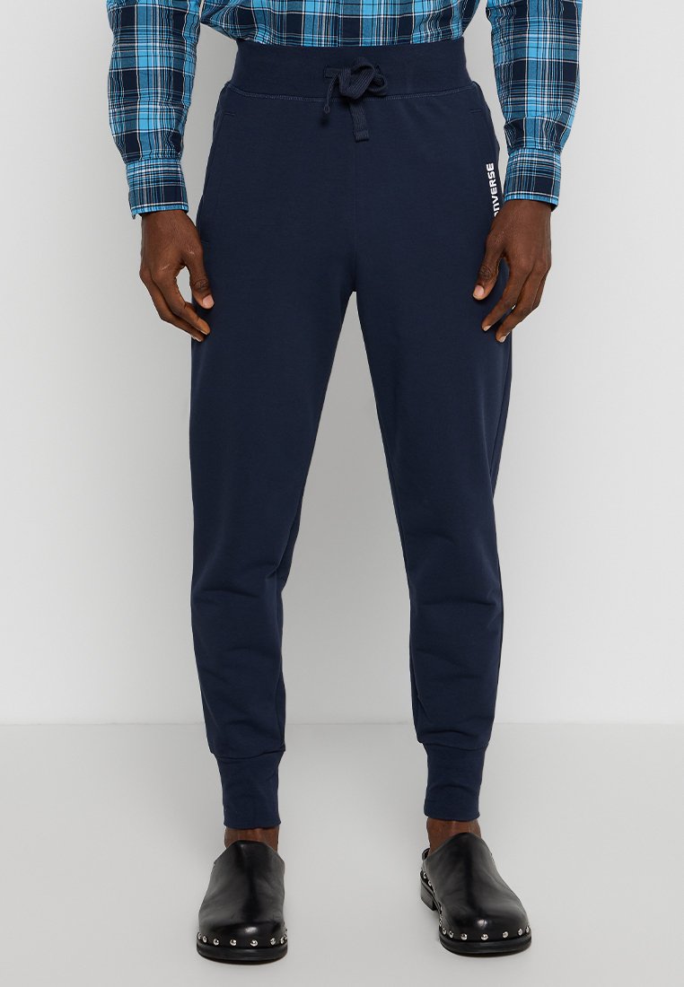 Pantaloni jogging blu navy con vita elastica e coulisse, dotati di polsini aderenti e branding laterale. Realizzati in tessuto morbido e traspirante.
