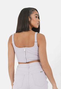 Top corto a coste lilla con spalline spesse e zip centrale sul retro. Il tessuto appare leggermente testurizzato e aderente.