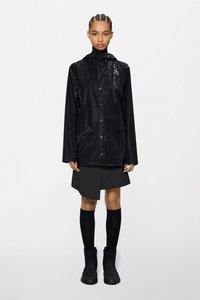 Μαύρο, γυαλιστερό αδιάβροχο μπουφάν με κουκούλα, κούμπωμα με κουμπιά και υφή, φορεμένο πάνω από σκουρόχρωμη φούστα και μαύρες κάλτσες μέχρι το γόνατο με μπότες.