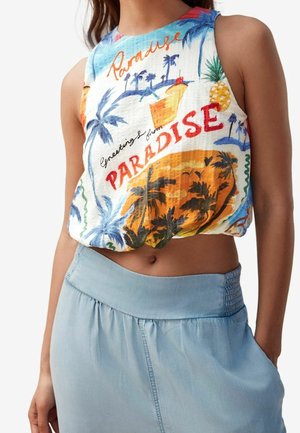 Bezrękawnik tropikalny crop top z motywami palm, ananasa, koktajlu i napisem "Pozdrowienia z raju", noszony z jasnoniebieską spódnicą.