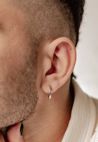 Orecchino a cerchio in argento indossato in un primo piano dell'orecchio, che mette in evidenza la superficie metallica liscia e il design minimalista contro capelli corti e texturizzati.