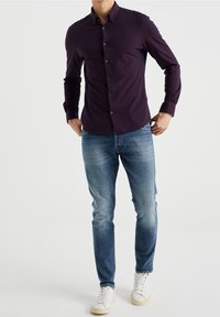 Tummanvioletti nappitaskullinen pitkähiha paita, yhdistetty vaaleanpesuisiin farkkuihin ja valkoisiin tennareihin. Paidassa on hillitty logo rintamuksella.