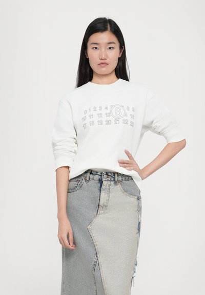 Felpa bianca con una grafica circolare che presenta numeri, abbinata a una gonna in denim patchwork a vita alta. Tessuto dalla consistenza liscia.