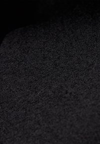 Gros plan d'un tissu noir texturé avec une surface douce et duveteuse et des fibres fines visibles sous l'éclairage.