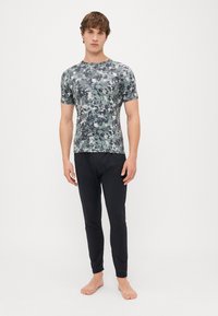 Mandens atletiske outfit består af en kortærmet top med camouflage-mønster i nuancer af grå og grøn, parret med tætsiddende sorte leggings.