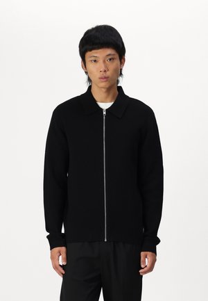 Schwarzer Reißverschluss-Pullover mit Kragen, langen Ärmeln, gerippten Bündchen und geradem Saum. Hergestellt aus einem weichen, strukturierten Stoff, der sich gut für das Lagenlayering eignet.