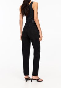 Jean noir taille haute à coupe droite, avec deux poches arrière et un design minimaliste. Porté avec des sandales noires à talons.