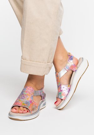 Multi-colored metallic sandals with an open design, silver accents, and a cushioned sole, paired with rolled-up beige corduroy pants.