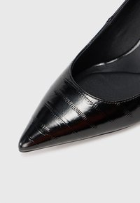Čierne lakkové lodičky s špičatou špičkou, ktoré majú štruktúrovaný vzor a hladký interiér. Dizajn je elegantný s modernou siluetou.