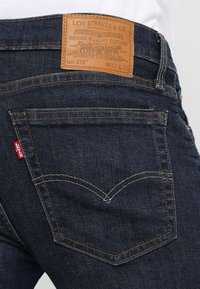 Vaqueros de mezclilla azul oscuro con un parche de cuero etiquetado "Levi Strauss & Co." en la parte trasera, con costuras características y dos bolsillos traseros.