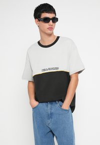 Κοντομάνικη μπλούζα με σχέδιο σε αποχρώσεις του γκρι και μαύρου, με αντίθετη κίτρινη ρίγα και το λογότυπο "BILLA BONG" στο στήθος.