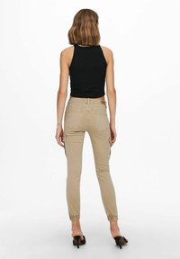Pantalones cargo beige con puños elásticos, múltiples bolsillos laterales y un ajuste de altura media. Combinados con una camiseta sin mangas de canalé negra.