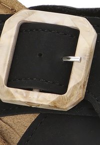 Sandalo in pelle nera con una tracolla che presenta una fibbia quadrata e texturizzata di colore chiaro con un perno metallico lucido.