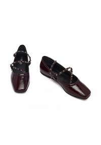 Chaussures en cuir verni bordeaux avec un bout carré, dotées de brides croisées ornées de clous décoratifs. Talon bas carré. Doublure intérieure noire.