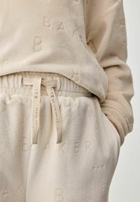 Beige sweatshirt og joggers med en blød, tekstureret finish, med prægede bogstaver og en snøre i taljen for justerbar pasform.