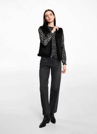 Svart ärmlös väst i texturerad tyg, lager på en blommönstrad långärmad skjorta, tillsammans med högmidjade svarta jeans och ankelstövlar.