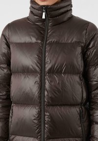 Dunkelbraune gepolsterte Jacke mit hohem Kragen, Frontreißverschluss und glänzender Stofftextur mit horizontalen Steppabschnitten.