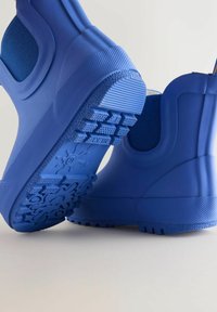 Mėlyni neperšlampami guminiai batai su tekstūruotu padu, turintys elastines šonines juostas ir lygią, patvarią apdailą.