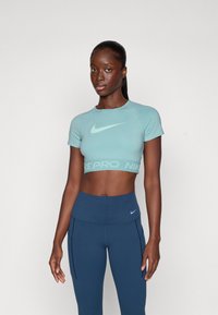 Top corto azul claro con un escote redondeado, mangas cortas y el logo de Nike; combinado con leggings oscuros de cintura alta con detalles en los laterales.