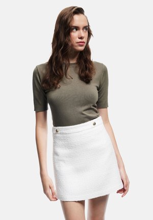 Vit texturerad minikjol med guldknappar, kombinerad med en figurnära olivgrön kortärmad topp. Enkel och ren design.