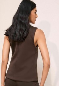 Brauner ärmelloser Top aus glattem Stoff, mit einer figurbetonten Passform und leichtem Glanz, sichtbaren Nahtdetails und einer klaren Silhouette.