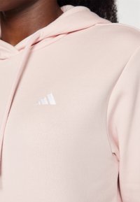 Sweatshirt rosa claro com uma textura suave, apresentando um logótipo bordado da Adidas em branco no peito e uma capuz clássico com cordões.