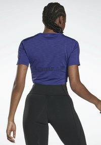 T-shirt d'athlétisme violet court avec des manches courtes et une finition texturée. Présente un logo noir "LES MILLS" au dos. Associe à un legging noir.