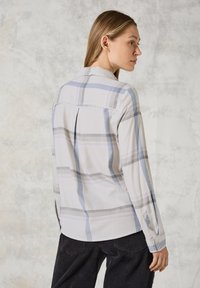Camicia a maniche lunghe in plaid in tonalità pastello di grigio, blu e viola. Tessuto morbido, con colletto, dettagli con piega e bottone sul retro.