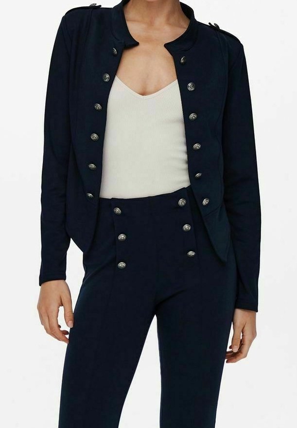 Blazer ajusté bleu marine avec col montant et boutons argentés, associé à un pantalon taille haute assorti avec boutons décoratifs.