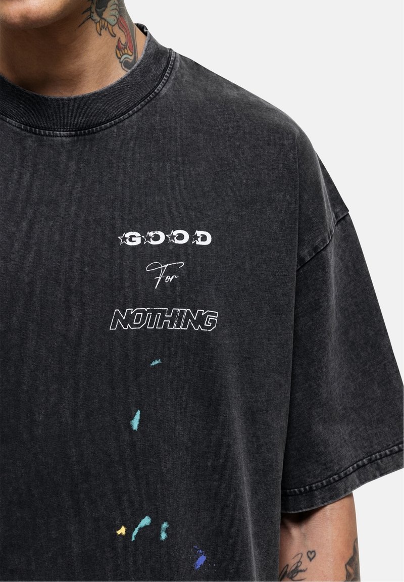 Musta oversize t-paita, jossa on pyöreä kaula-aukko, näyttävä valkoinen graafinen printti ja värikkäitä roiskeita, valmistettu pehmeästä ja teksturoidusta kankaasta.