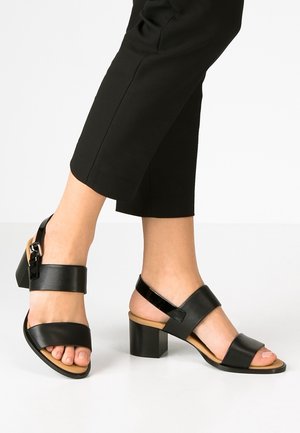 Czarne skórzane sandały z dwoma szerokimi paskami, masywnym obcasem typu blok oraz zapięciem na klamrę. Gładka faktura o neutralnym kolorze bazowym.