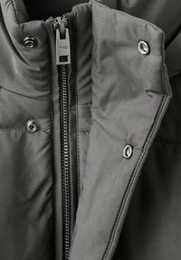 Chaqueta acolchada gris con cierre de cremallera y botones de presión, que presenta una textura suave y un diseño acolchado para aislamiento.