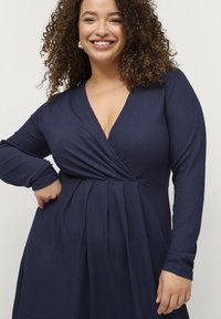 Marineblaue, strukturierte Wickelkleid mit langen Ärmeln, V-Ausschnitt und gerafftem Taillenbereich, das ein fließendes Rockdesign aufweist.