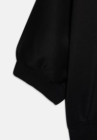 Manga de tela negra con puño acanalado, que muestra un material texturizado y detalles de costura sobre un fondo blanco liso.
