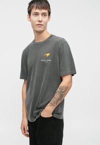 Graues Baumwoll-T-Shirt mit grafischem Druck "AUSTIN, TEXAS 2025" in Weiß und einem orangenen Akzent. Lässige Passform, kurze Ärmel.