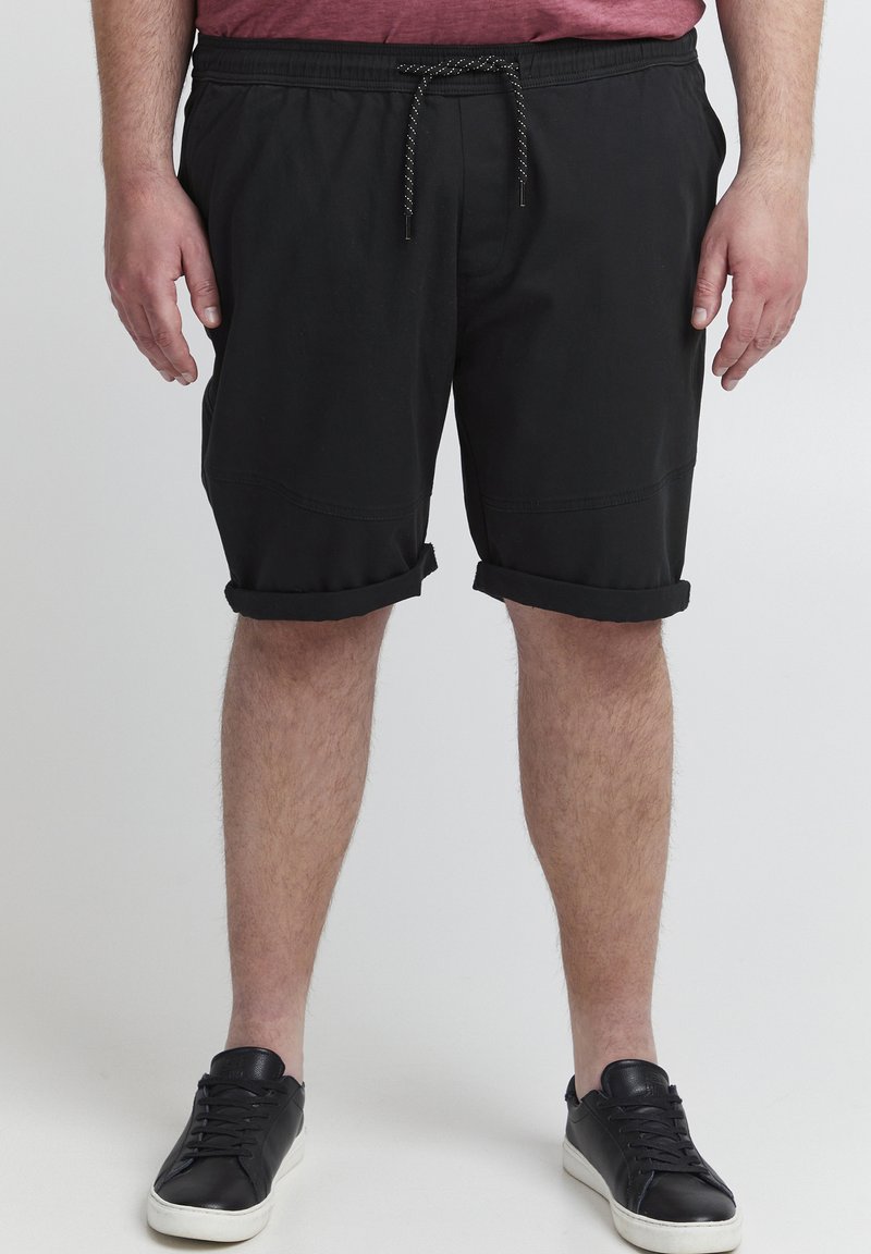 Sorte shorts med elastisk midjebånd og snor, med rullet kant og glattet stofftekstur, kombinert med svarte sneakers.