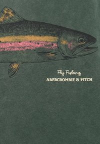 Oliivinvihreä t-paita, jossa on yksityiskohtainen graafinen kuvitus kalasta, jossa on vaaleanpunaisia ja keltaisia yksityiskohtia, sekä teksti "Fly Fishing Abercrombie & Fitch."