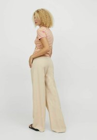 Top a righe maniche corte in rosa e giallo; pantaloni beige a gamba larga con una texture morbida e una vestibilità ampia; sandali flat neri. Vista posteriore.