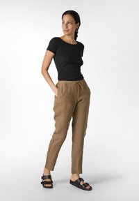 Svart kortärmad åtsittande topp, bruna linnebyxor med dragsnöre och svarta sandaler med dubbelrem. Enkel, avslappnad passform med sidofickor.